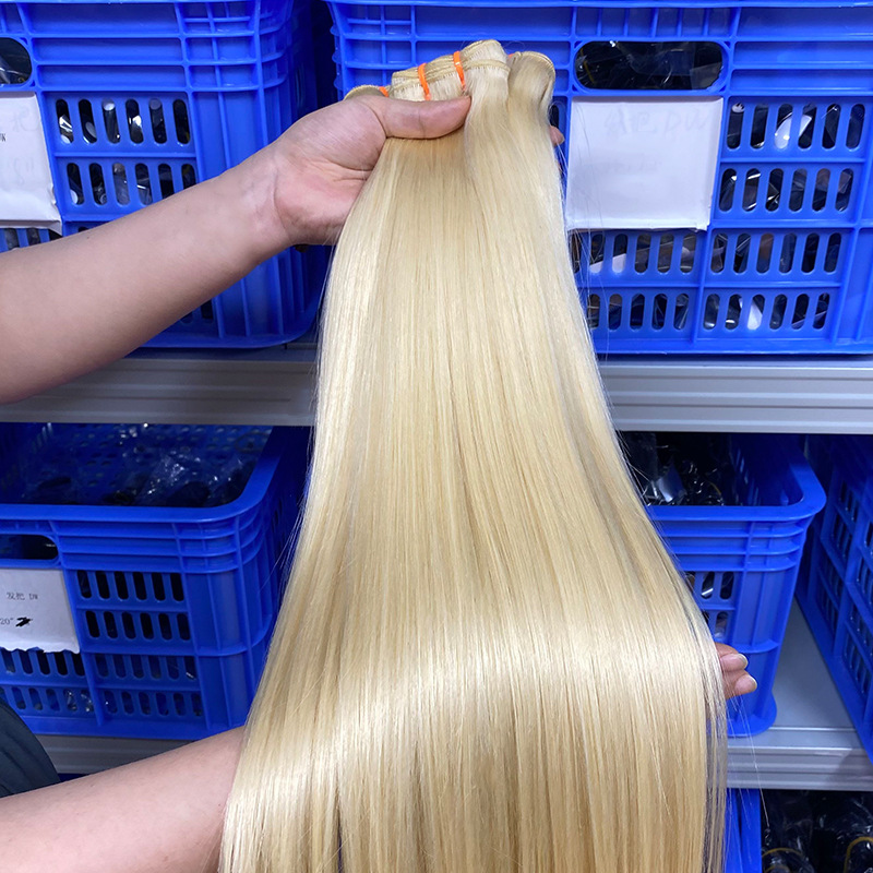 Scarlett Hair Hand holding bundle of straight blonde hair extensions in front of blue storage bins